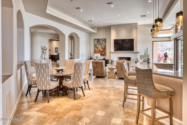 dining space with visible vents, recessed lighting, arched walkways, a fireplace, and stone tile flooring