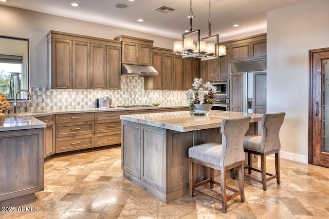 kitchen featuring under cabinet range hood, a sink, a kitchen island, decorative backsplash, and built in appliances