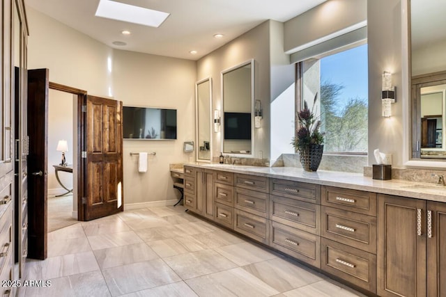 full bath featuring double vanity, a skylight, and a sink