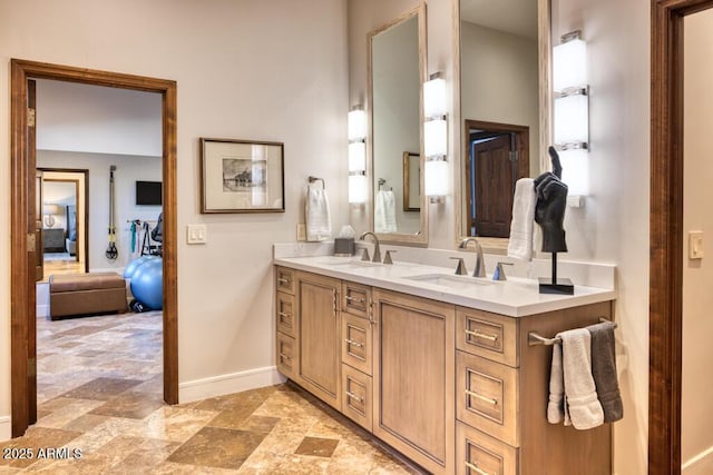 ensuite bathroom with a sink, connected bathroom, baseboards, and double vanity