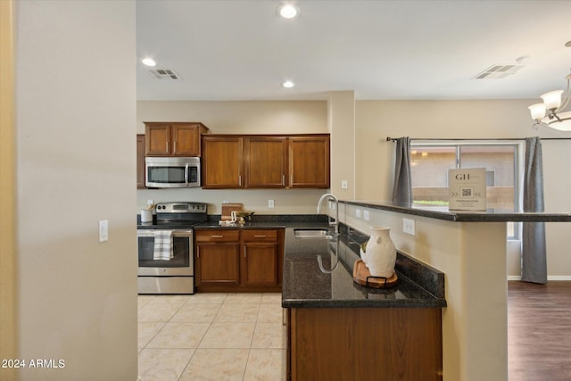 kitchen with appliances with stainless steel finishes, sink, hanging light fixtures, light hardwood / wood-style floors, and dark stone countertops