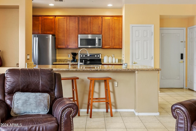 kitchen with light tile patterned floors, a kitchen bar, light stone counters, and stainless steel appliances