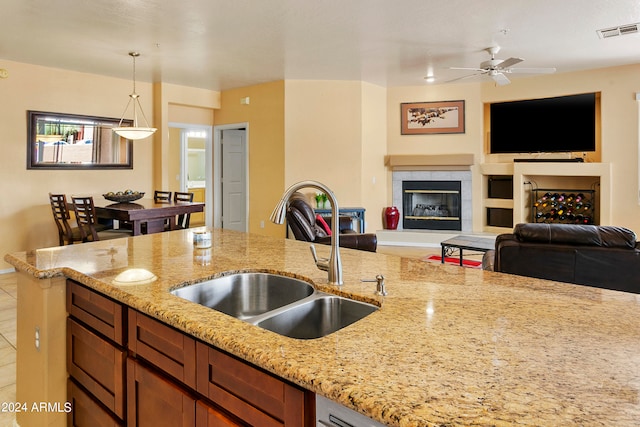 kitchen with tile patterned floors, a tile fireplace, light stone counters, sink, and ceiling fan