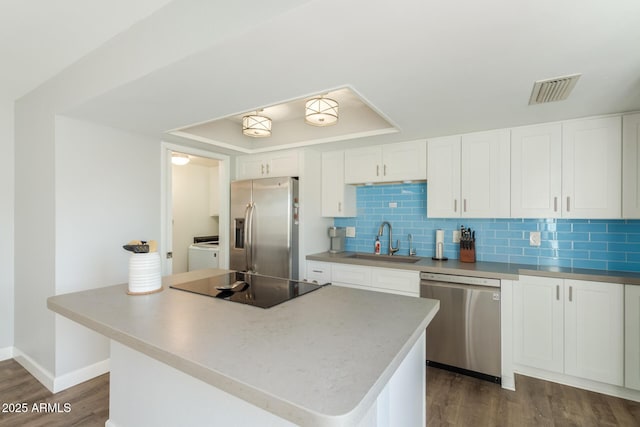 kitchen with appliances with stainless steel finishes, a sink, dark wood-type flooring, white cabinetry, and washer and dryer