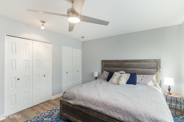 bedroom featuring wood finished floors, two closets, ceiling fan, and baseboards