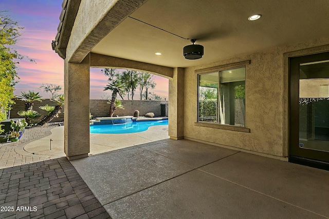 pool at dusk featuring ceiling fan and a patio area