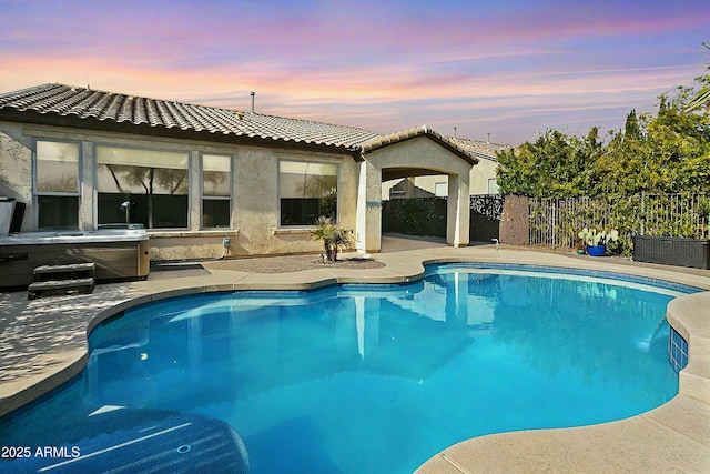 pool at dusk with a hot tub and a patio