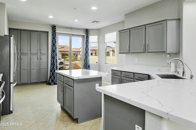 kitchen with a kitchen island, sink, gray cabinetry, stainless steel fridge, and light stone counters