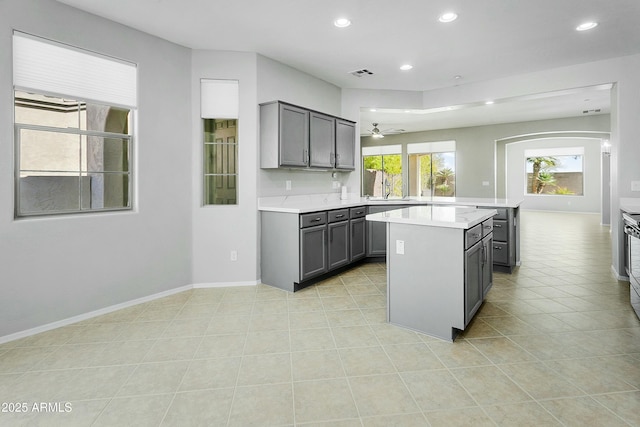 kitchen featuring gray cabinets, light tile patterned flooring, sink, a center island, and ceiling fan