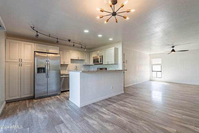 kitchen with white cabinets, light stone countertops, tasteful backsplash, appliances with stainless steel finishes, and light wood-type flooring