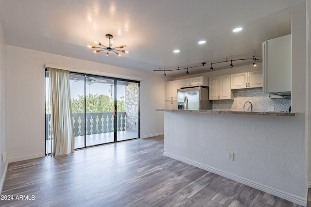 kitchen with stainless steel fridge, kitchen peninsula, light stone counters, and white cabinets