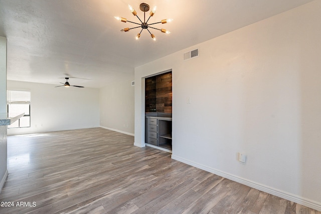 empty room featuring ceiling fan with notable chandelier and light hardwood / wood-style flooring