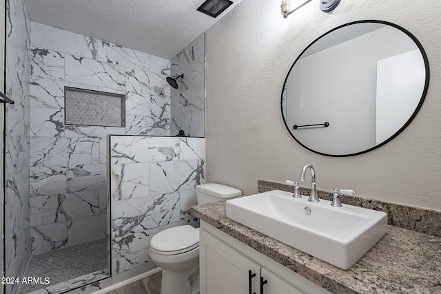 bathroom with a textured ceiling, a tile shower, vanity, and toilet