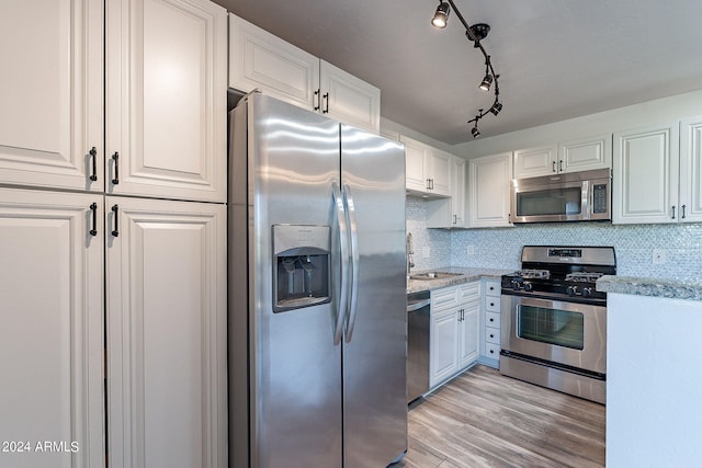 kitchen with appliances with stainless steel finishes, light wood-type flooring, light stone countertops, and white cabinets