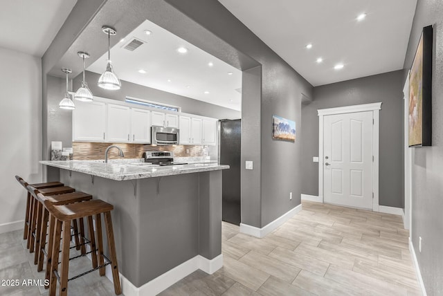 kitchen featuring visible vents, backsplash, stainless steel appliances, a peninsula, and white cabinets