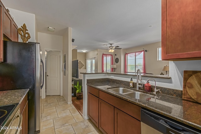 kitchen featuring ceiling fan, kitchen peninsula, sink, appliances with stainless steel finishes, and dark stone countertops