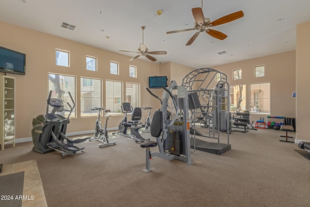 workout area featuring ceiling fan, a towering ceiling, and light carpet