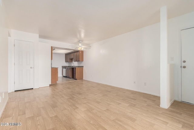 unfurnished living room featuring ceiling fan, light wood-style floors, baseboards, and a sink