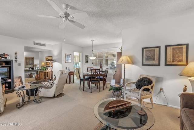 living room featuring ceiling fan, visible vents, a textured ceiling, and light colored carpet