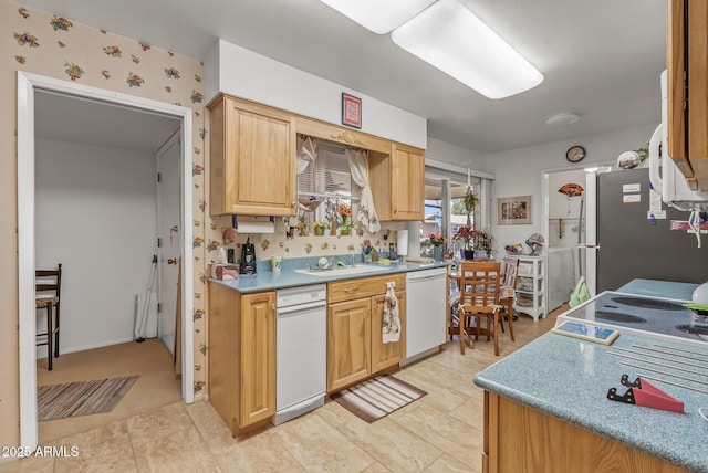 kitchen with cooktop, light countertops, freestanding refrigerator, white dishwasher, and a sink