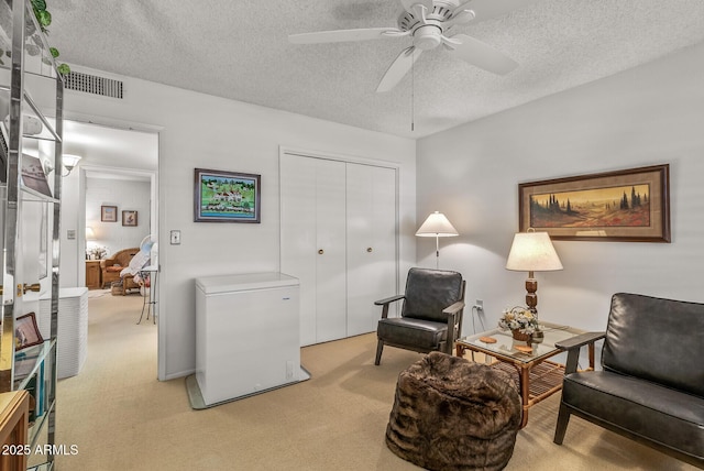 living area with light carpet, ceiling fan, visible vents, and a textured ceiling