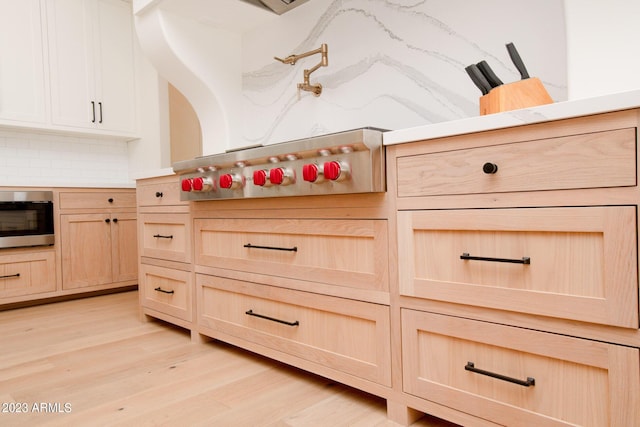 interior space with tasteful backsplash, cooktop, stainless steel microwave, light brown cabinets, and light wood-type flooring