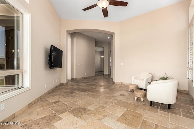 interior space with arched walkways, baseboards, stone tile flooring, and ceiling fan