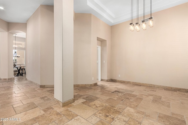 unfurnished room featuring a tray ceiling, arched walkways, baseboards, and stone tile flooring