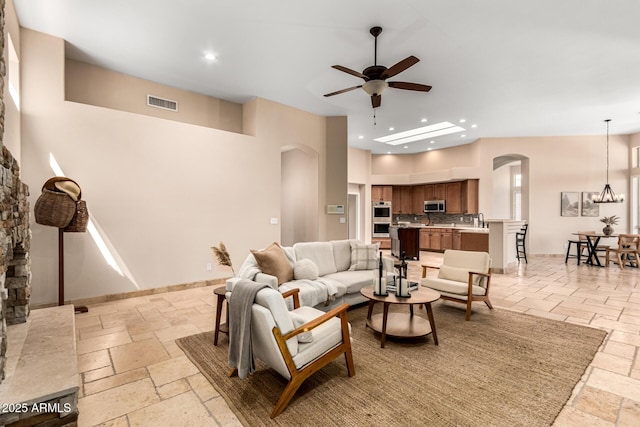 living area featuring stone tile flooring, ceiling fan, arched walkways, and visible vents