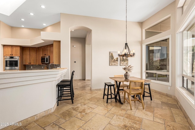 kitchen with brown cabinets, decorative backsplash, stainless steel appliances, arched walkways, and stone tile floors