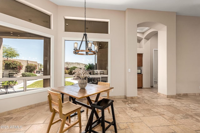dining space featuring baseboards, arched walkways, a high ceiling, a chandelier, and stone tile floors