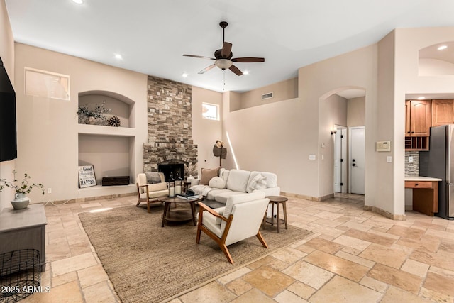 living room with arched walkways, stone tile floors, a ceiling fan, a stone fireplace, and baseboards