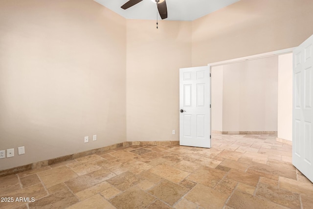 unfurnished room with stone tile flooring, baseboards, a ceiling fan, and a towering ceiling