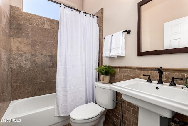 full bath featuring a wainscoted wall, toilet, shower / bath combo, a sink, and tile walls