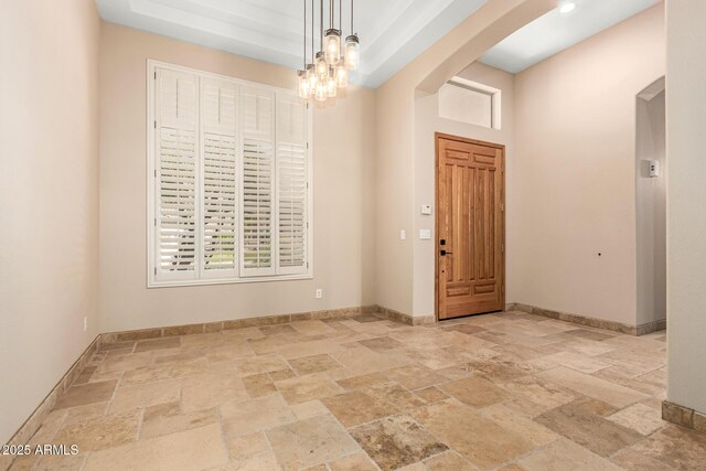 empty room with baseboards, arched walkways, an inviting chandelier, and stone tile floors