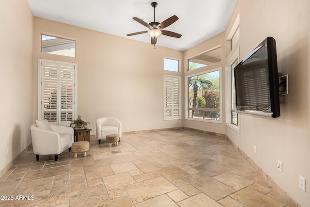 living area with stone tile floors, ceiling fan, and baseboards