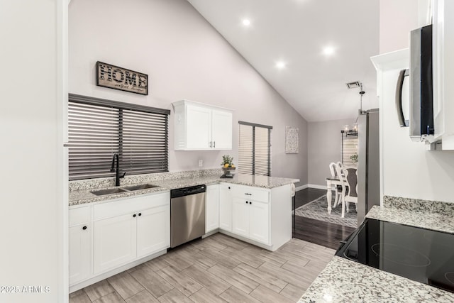 kitchen with wood finish floors, appliances with stainless steel finishes, white cabinets, a sink, and a peninsula