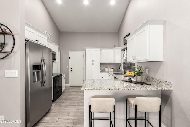 kitchen featuring light stone counters, a peninsula, a sink, white cabinetry, and appliances with stainless steel finishes