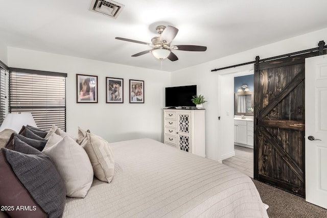 carpeted bedroom with a barn door, visible vents, a ceiling fan, ensuite bath, and a sink