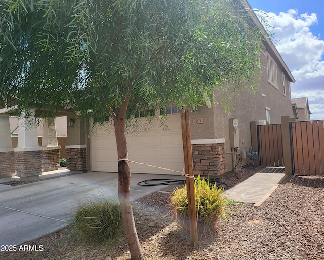 view of side of property with a gate, stone siding, driveway, and stucco siding