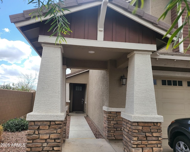 entrance to property featuring stone siding, stucco siding, a garage, and fence