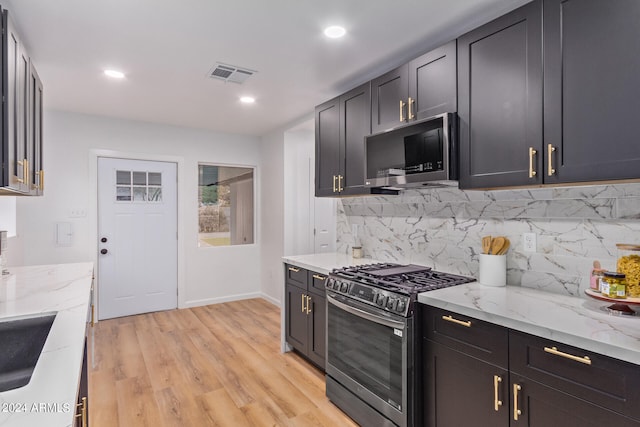 kitchen with appliances with stainless steel finishes, light hardwood / wood-style floors, light stone countertops, and decorative backsplash