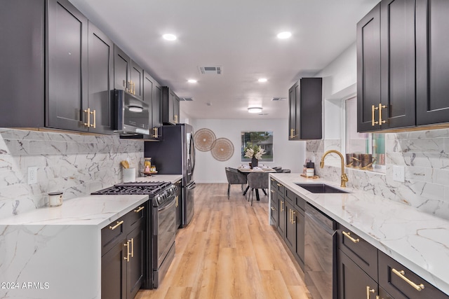 kitchen featuring tasteful backsplash, light hardwood / wood-style flooring, sink, light stone countertops, and appliances with stainless steel finishes