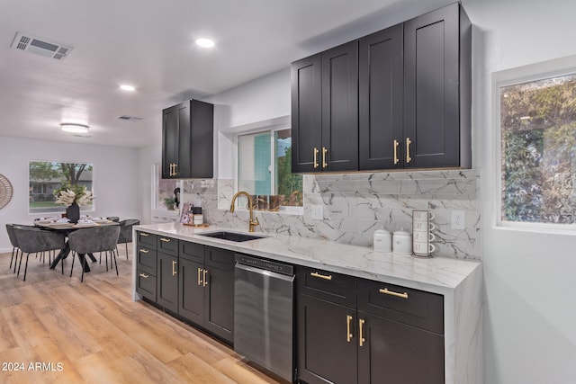 kitchen featuring tasteful backsplash, light stone counters, sink, stainless steel dishwasher, and light hardwood / wood-style floors