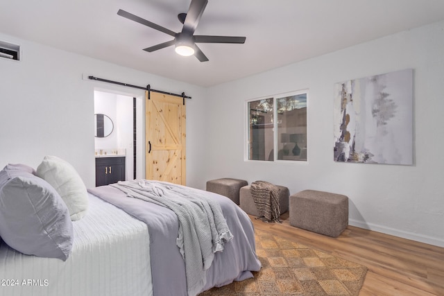 bedroom with a barn door, hardwood / wood-style floors, ceiling fan, and ensuite bath