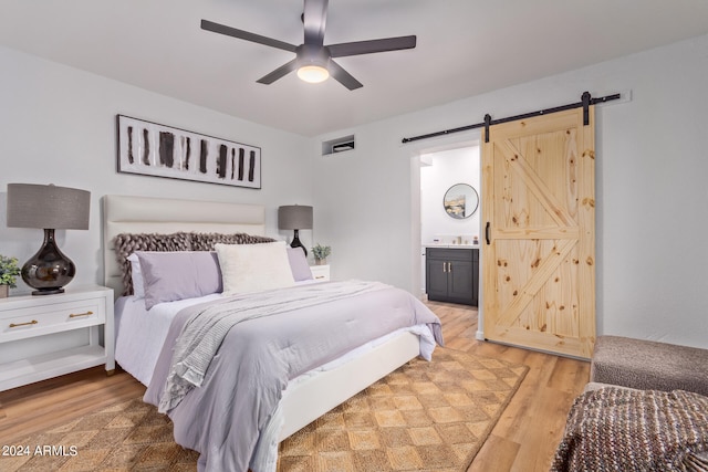 bedroom with connected bathroom, hardwood / wood-style floors, ceiling fan, and a barn door