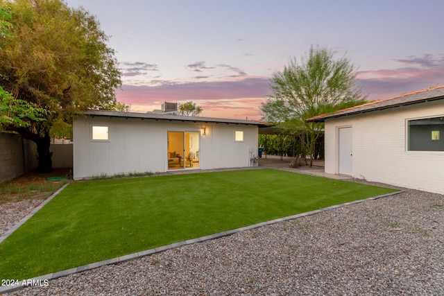 back house at dusk with a patio area and a lawn