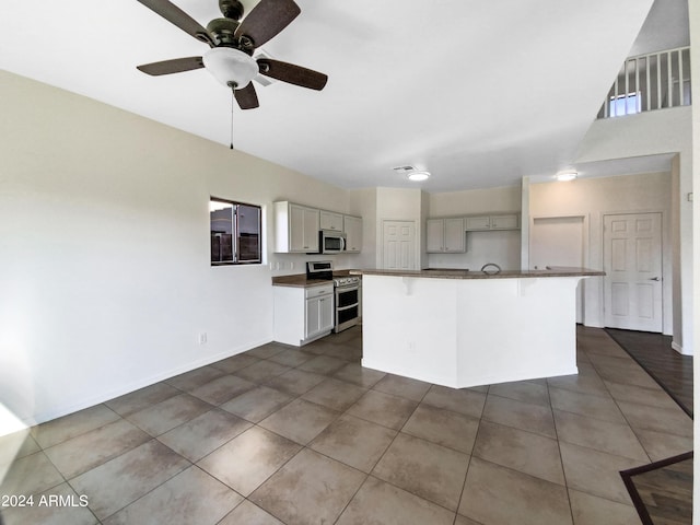 kitchen featuring dark tile patterned flooring, a kitchen island with sink, stainless steel appliances, dark countertops, and a kitchen breakfast bar