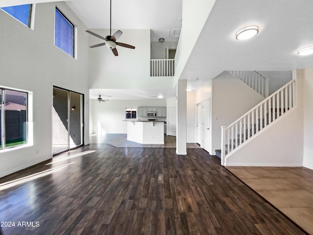 unfurnished living room with a ceiling fan, dark wood-style floors, baseboards, a towering ceiling, and stairs