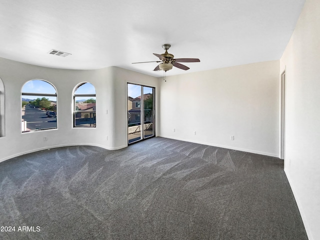 spare room featuring dark colored carpet, visible vents, a healthy amount of sunlight, and a ceiling fan